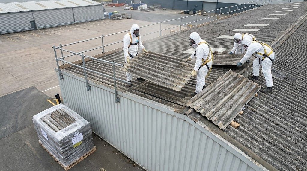 Arbeiter in Schutzanzügen bauen Asbestzement-Wellplatten von einem Hallendach zurück